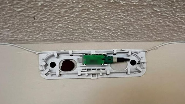 Open Primex box at the ceiling line with a green fiber connector seated, the unit marking obscured