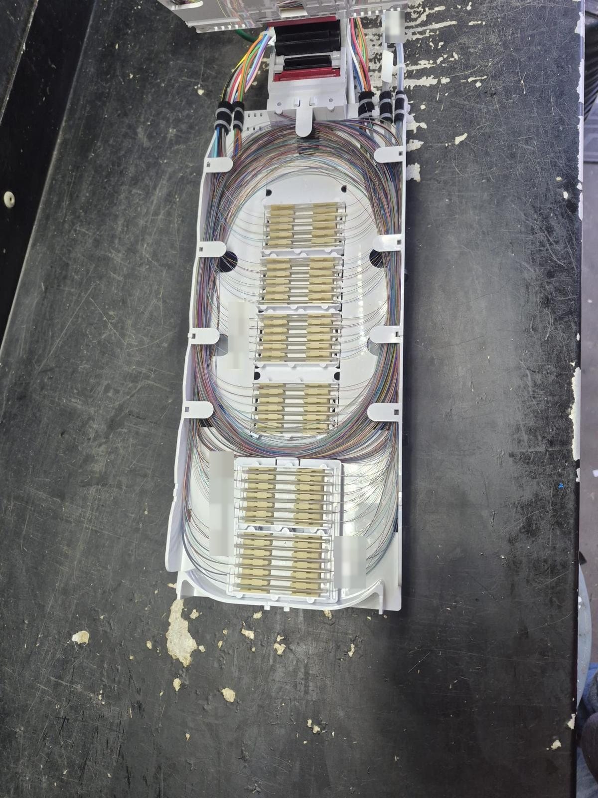 Splice tray with rows of protected fiber splices and neatly looped colour-coded fibers, with labels obscured