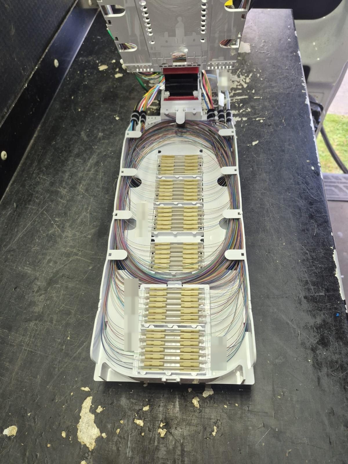 Completed fiber splice tray lifted from its closure, with rows of splices and organized fiber loops, with labels obscured