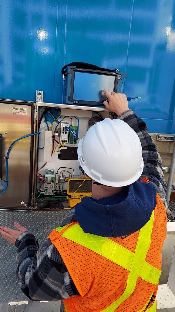 Technician using a portable EXFO OTDR at an open equipment cabinet
